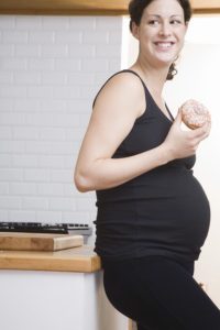 Pregnant woman eating doughnut in kitchen